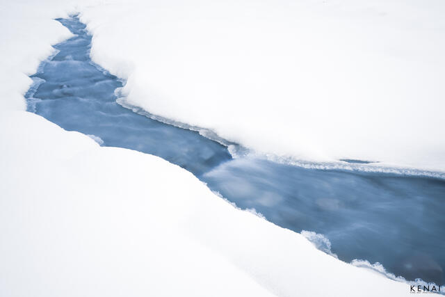 A stream of water cuts through deep snow in the winter of Alaska, near Black Rapids Glacier. 