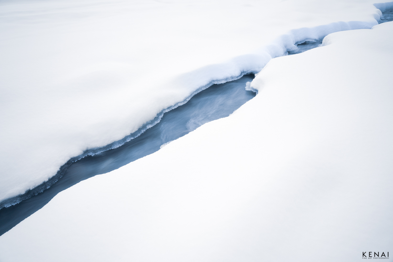 A small stream of water cuts through deep snow in the winter of Alaska, near Black Rapids Glacier.