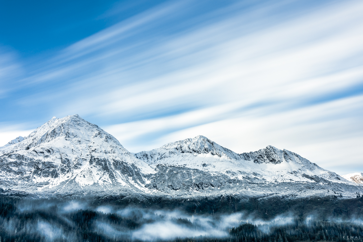 Clouds blur the blue sky in this long exposure photo of mountains near Valdez, Alaska